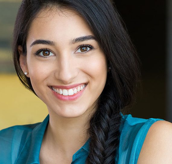 Smiling woman with braided black hair wearing blue top against yellow background