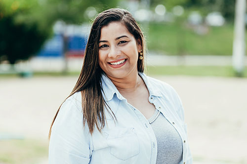 Woman smiling at camera wearing light blue shirt outdoors in park setting