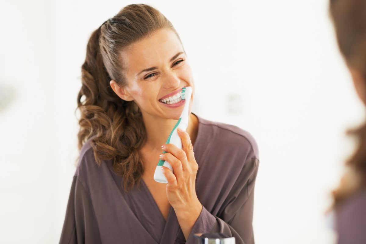 Woman applying toothpaste to toothbrush, smiling against white background.