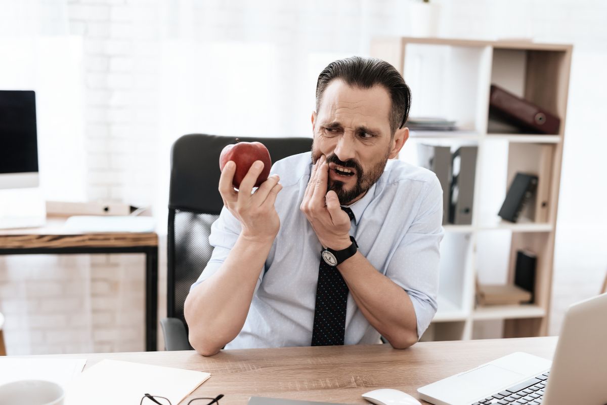 Man in office holding red apple, sitting at desk in business casual attire