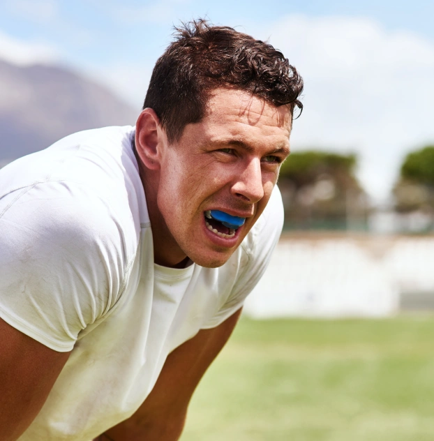 Male athlete outdoors wearing a blue custom athletic mouthguard.