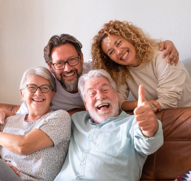 A happy multi-generational family smiling together, with a senior man giving a thumbs-up in the foreground.