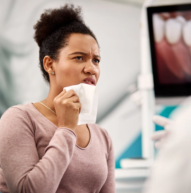 Woman holding a tissue to her face while experiencing discomfort from dry mouth symptoms.