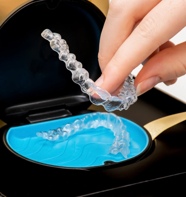 Hand placing a clear Invisalign aligner tray into its protective blue storage case.