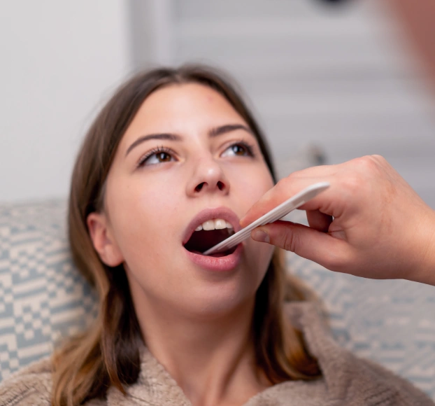 Dentist using a tongue depressor to perform an oral exam on a female patient.