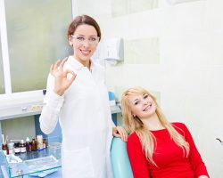 Dentist in white coat waving at patient in red shirt in dental office.